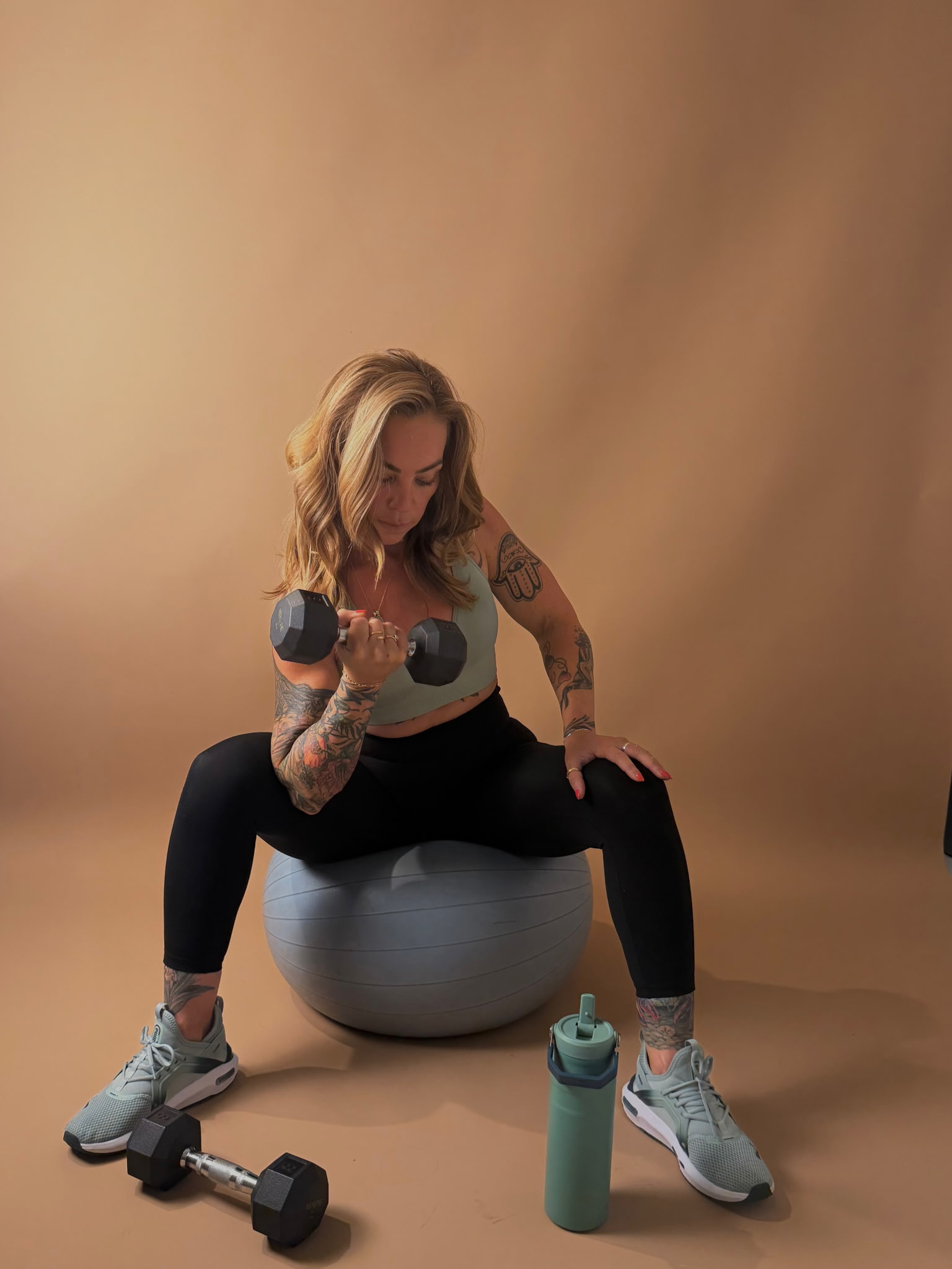 Belle performing a dumbbell curl in a warm editorial studio setting.
